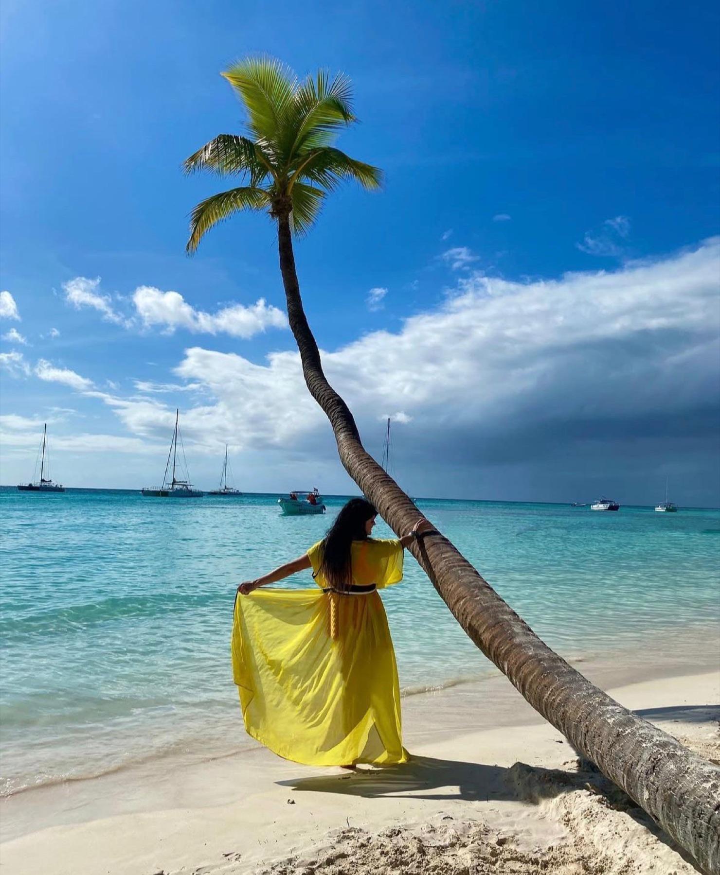 A guest in yellow beside a leaning palm and turquoise sea
